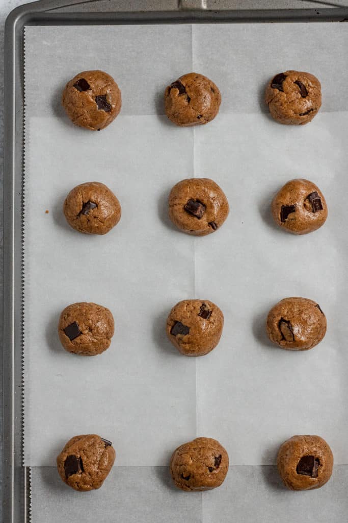 Chocolate chip cookie dough balls placed on a lined baking sheet ready to bake.