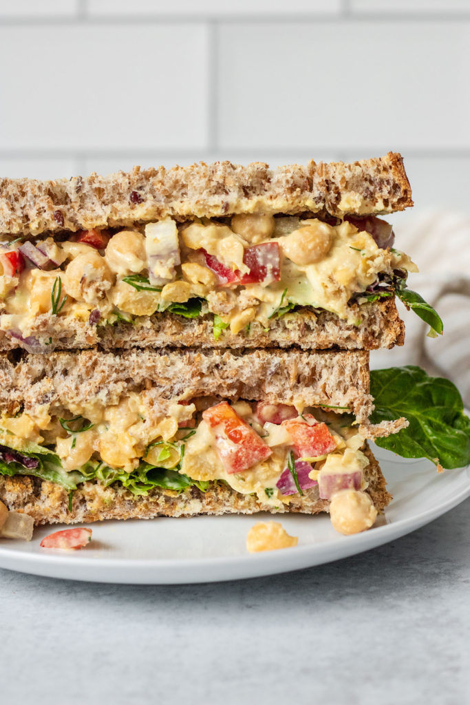 Close up of chickpea salad sandwich cut in half on a plate.