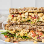 Chickpea salad sandwich plated with greens in between whole wheat bread.