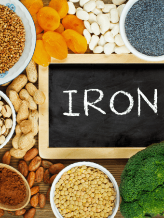 Beans, nuts, dried fruit, broccoli, chia seeds, whole grains and lentils surrounding a black board with the word iron written on it.