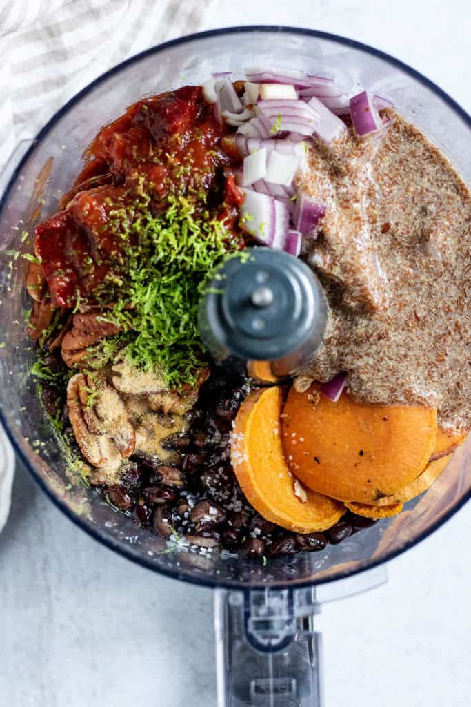 Food processor with sweet potatoes, black beans, oats, pecans, chipotle peppers and lime zest.