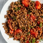 Garlic roasted lentils and tomatoes plated and topped with fresh dill and capers.