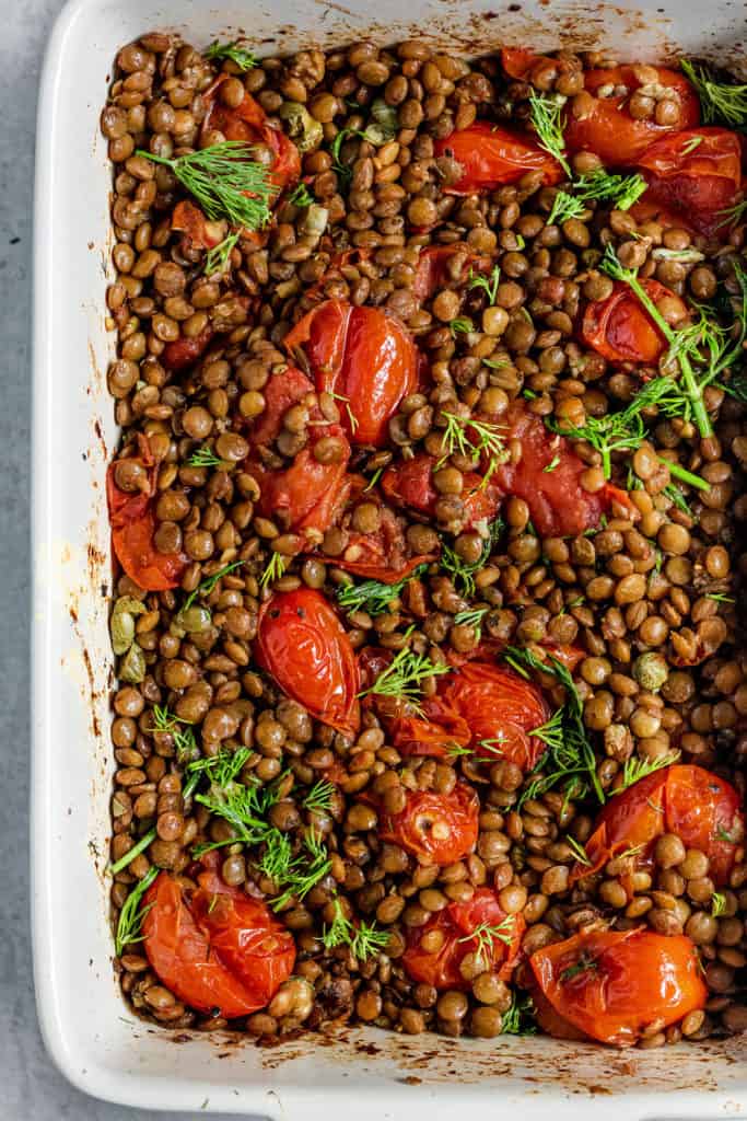 Close up of a baking dish with roasted tomatoes, lentils and fresh dill.
