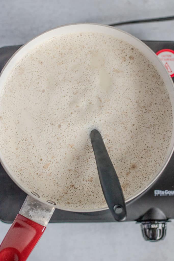 Adding oats to the boiling milk mixture while stirring.