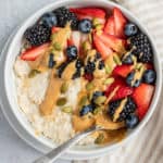 Oats in a white bowl topped with berries, peanut butter and maple syrup.