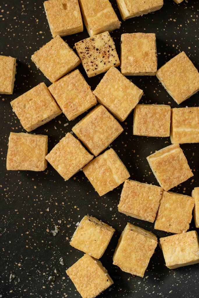 Crispy tofu being cooked in a black pan.