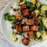 Glossy tofu plated with brussel sprouts and rice on a white plate.