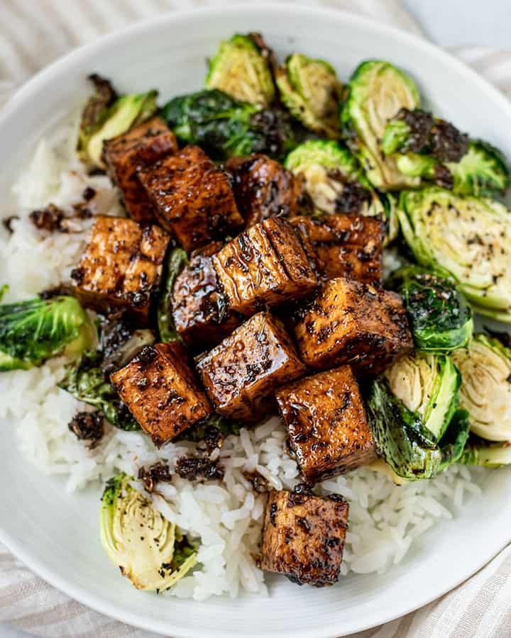 Plate of rice and brussel sprouts topped with glossy balsamic tofu.
