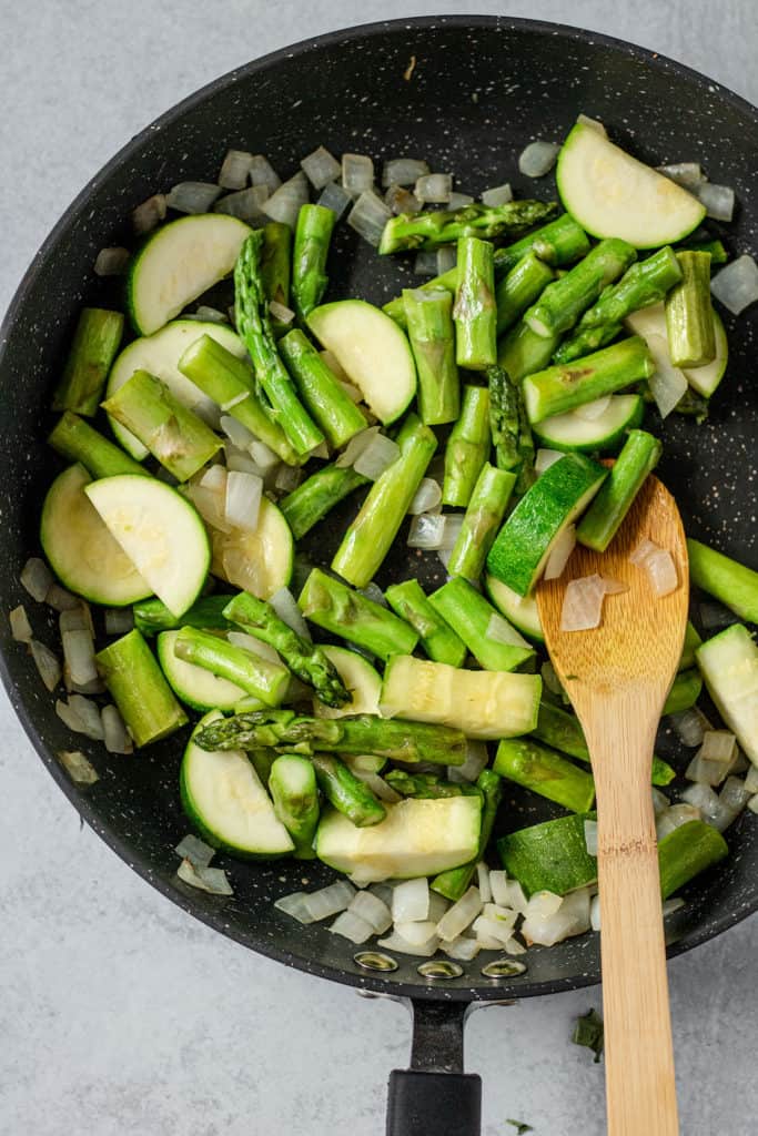 Sautéing zucchini, asparagus and onion together in a large sauté pan.