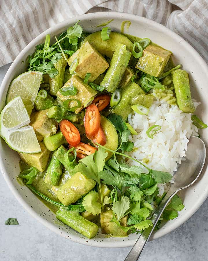 Clos up of green curry bowl served with rice and a spoon tucked in.