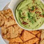 Close up view of the avocado dip sprinkled with crushed red pepper and cilantro surrounded by pita crackers.