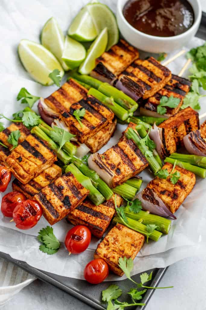 A tray of grilled tofu skewers topped with cilantro and a side of lime wedges.