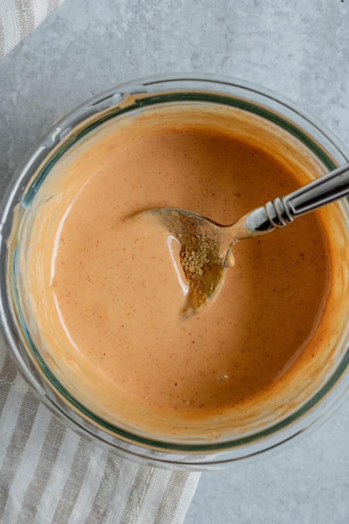 Glass bowl with creamy sriracha ginger sauce being mixed with a spoon.