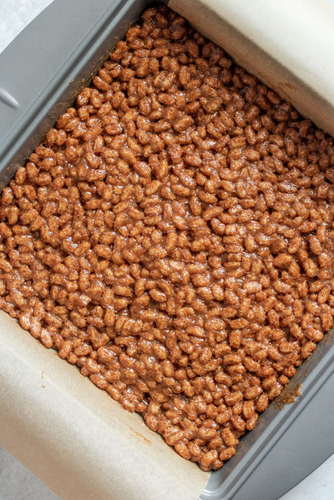 Rice crispy mixture being packed together in a baking pan.