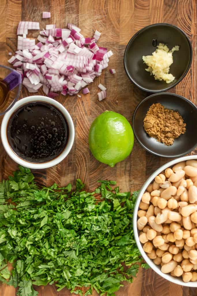 Cutting board topped with diced onion, lime, garlic, spices, beans and cilantro.