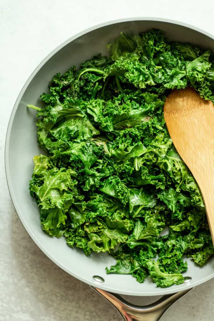Sautéed kale being cooked in a sauté pan with a spoon.