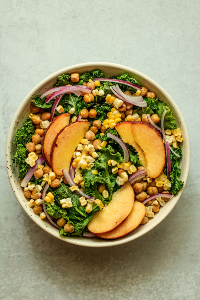 Kale and chickpeas being topped with peaches, corn, and onions.