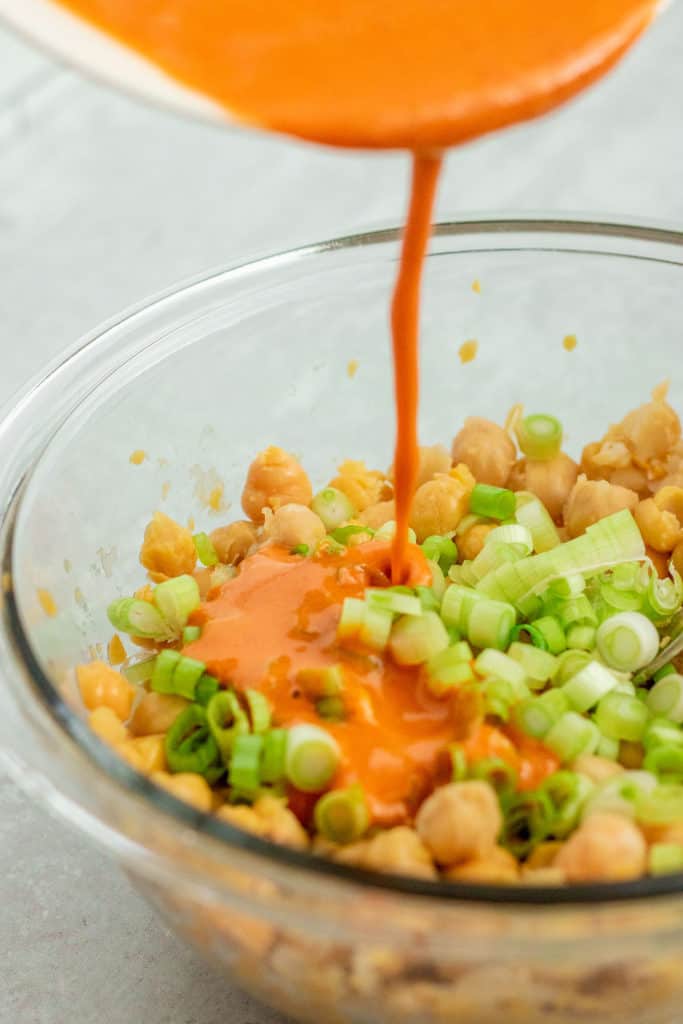 Peanut curry sauce being poured over the chickpeas and scallions.