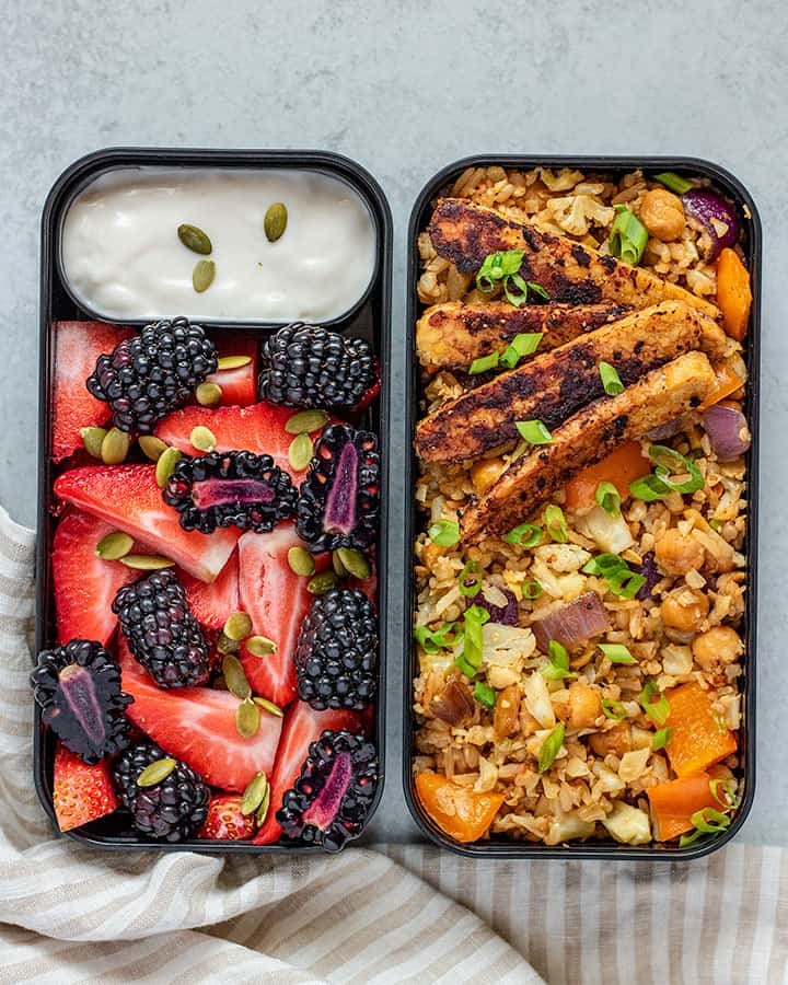 Close up of the bento boxes filled with fried rice and tempeh with a separate box filled with fruit and yogurt.