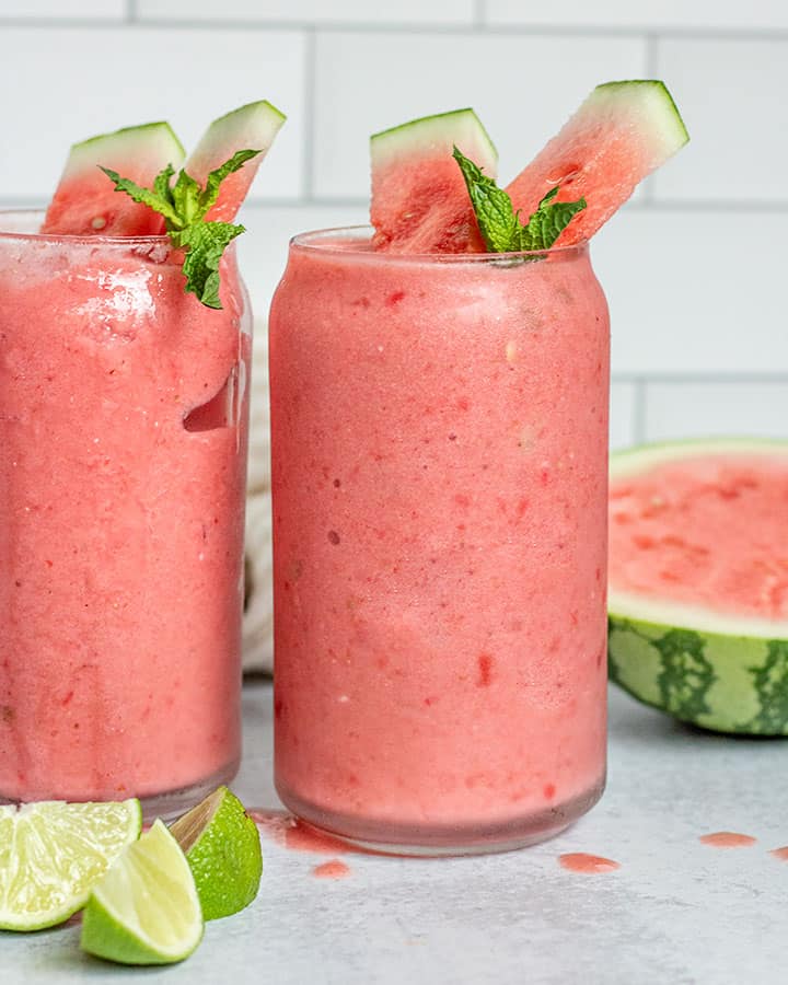 Two tall glasses of watermelon smoothie sitting next to each other.