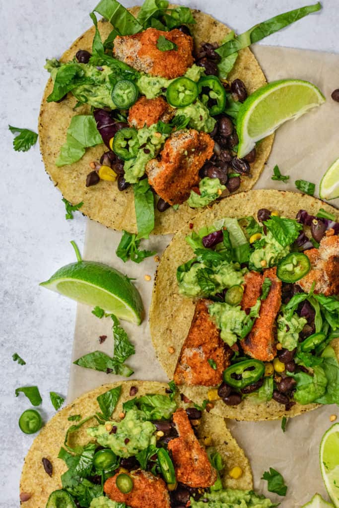 Picture of 3 tacos laying flat covered in beans, cauliflower bites, avocado and greens.