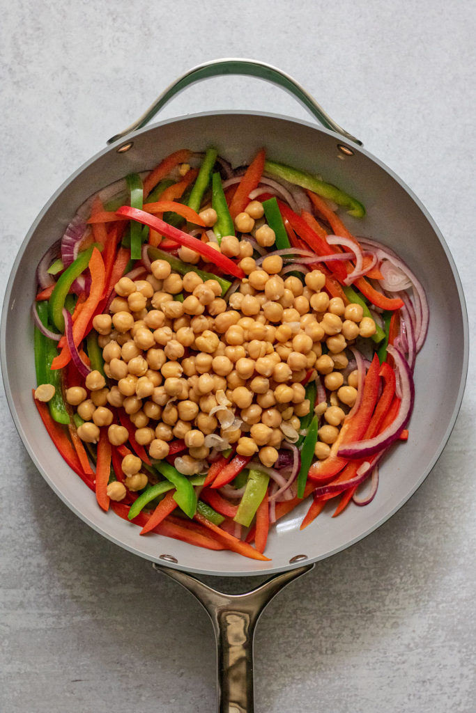 Sautéed peppers and onions, chickpeas in a large pan.