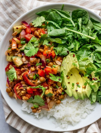 Close up of spiced lentils paired with rice, greens, avocado and fresh cilantro and chives.