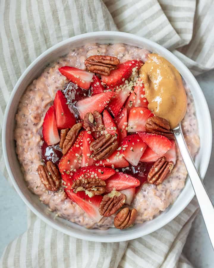 Close up on the oats with jam, strawberries, pecans and nut butter.