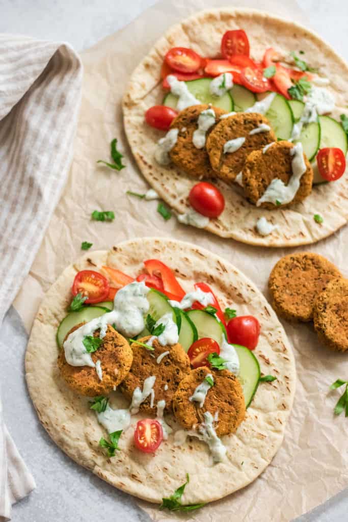 Picture of two pitas topped with chickpea patties and served with raw veggies and yogurt sauce.