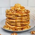 Stack of pancakes with a drizzle of maple syrup and walnuts sprinkled around it.