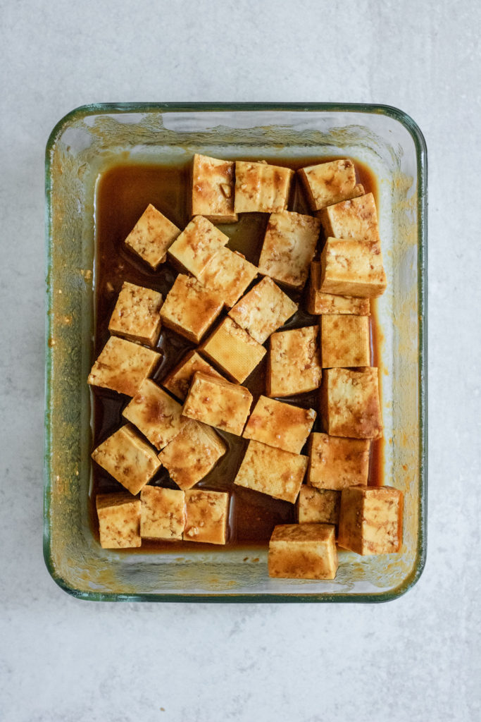 Tofu marinating in a sweet hoisin sauce in a glass container.