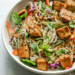 Close up of noodles topped with tofu and fresh herbs.