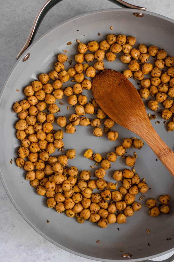 Chickpeas being toasted in a large skillet with adobo seasonings and fennel.