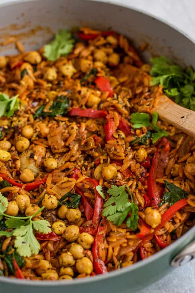 Skillet with fully cooked seasoned orzo, chickpeas and vegetables topped with fresh cilantro.
