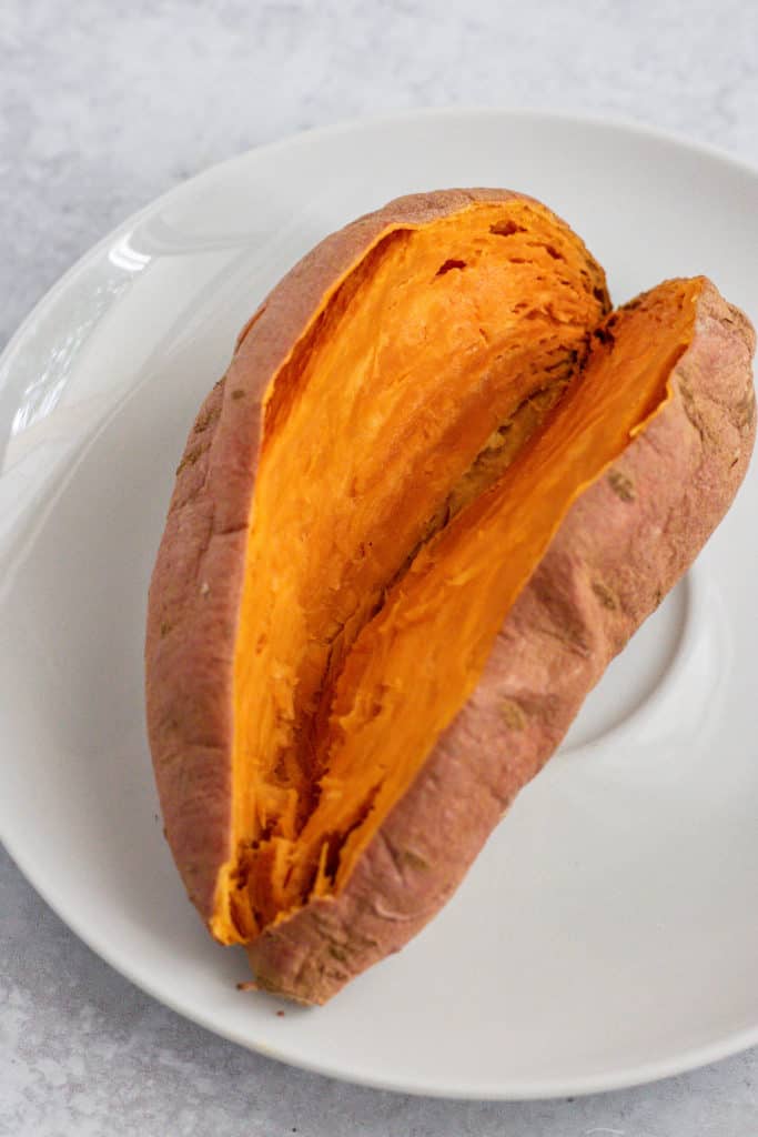Cooked sweet potato cut in half on a white plate.