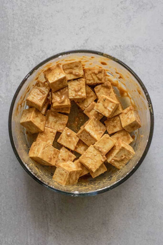 Tofu being mixed together in bowl with mso mustard sauce.