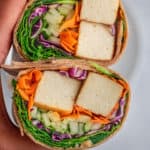 A wrap cut in half with tofu, vegetables held in hand.