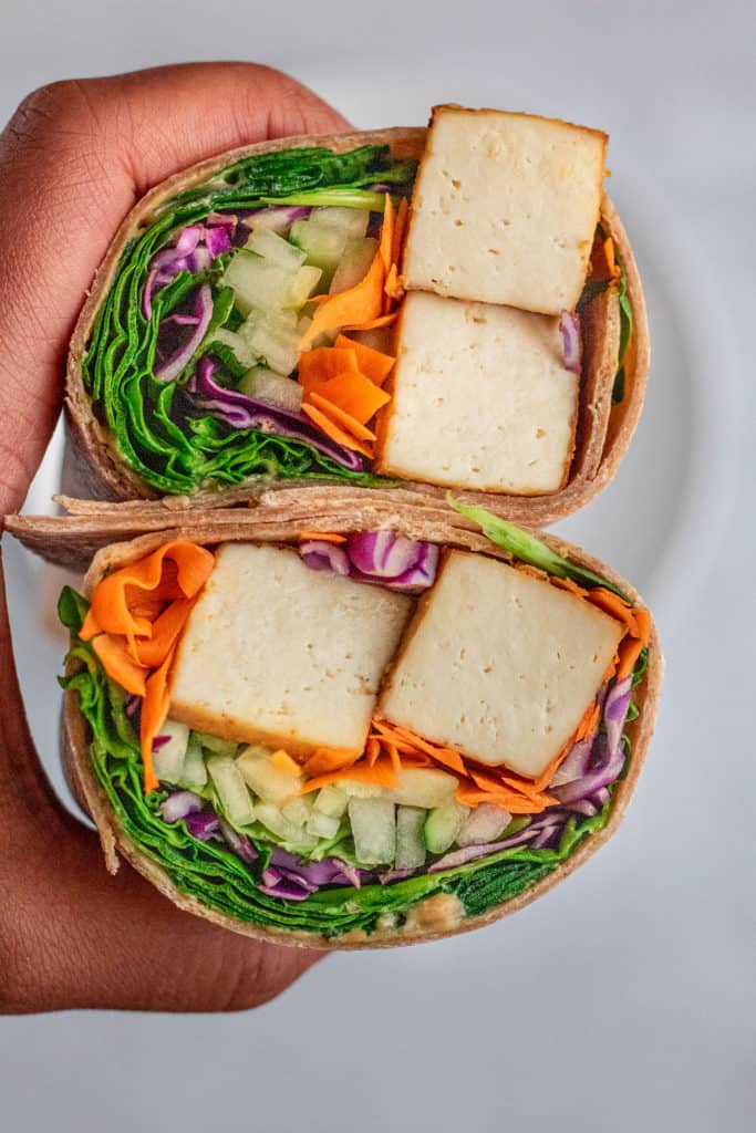 A wrap cut in half with tofu, vegetables held in hand.