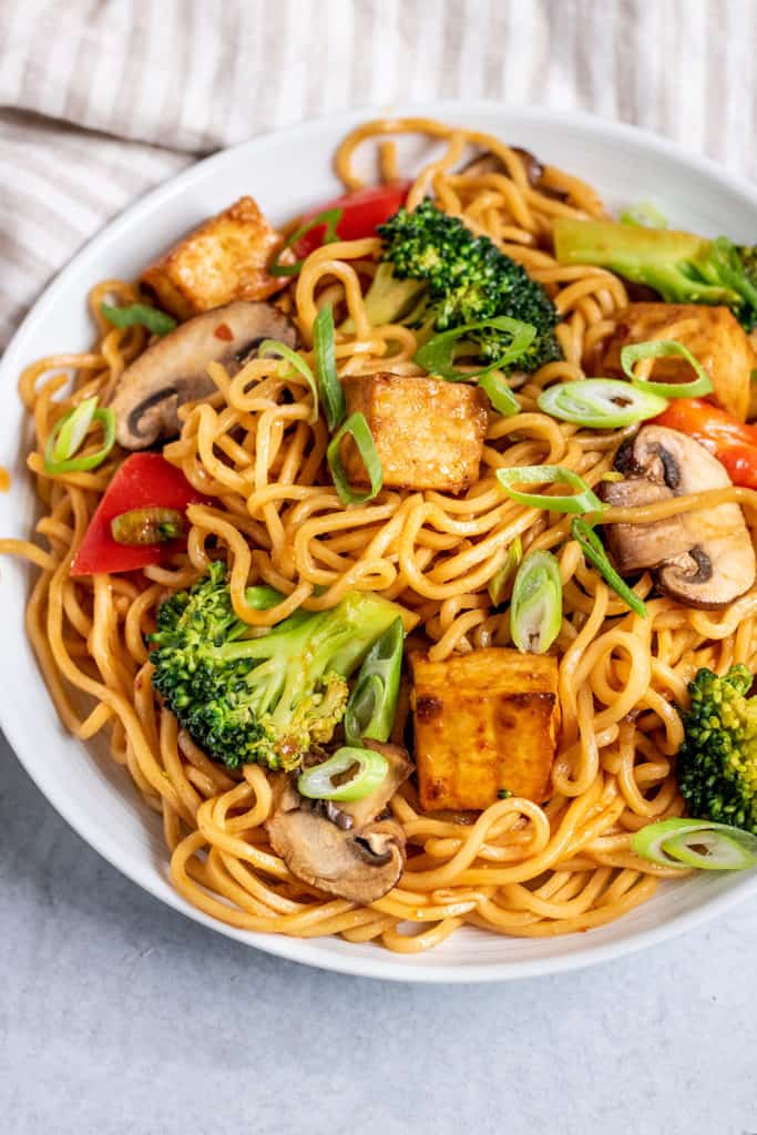 Side view of a plate of sriracha noodles tossed with tofu and vegetables.