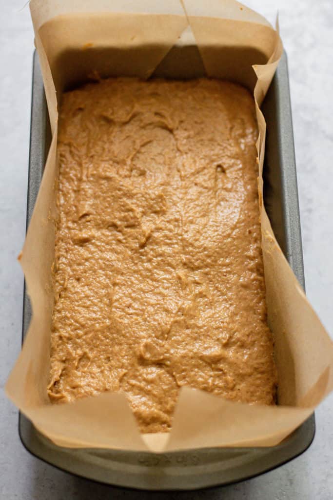 Batter being spread out evenly in a loaf pan lined with parchment paper.