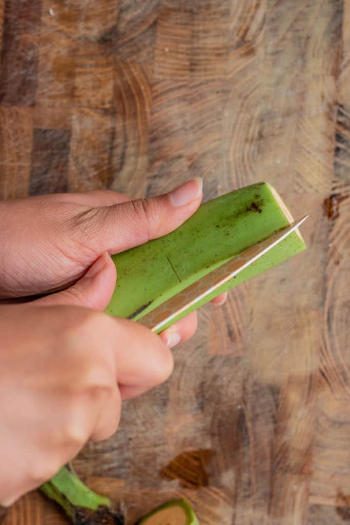 Using a paring knife to cut down the seem of a plantain.