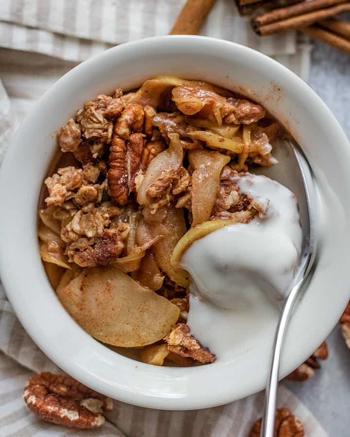 Close up shot of a small white bowl of baked apple oatmeal topped with a few spoons of vegan yogurt.