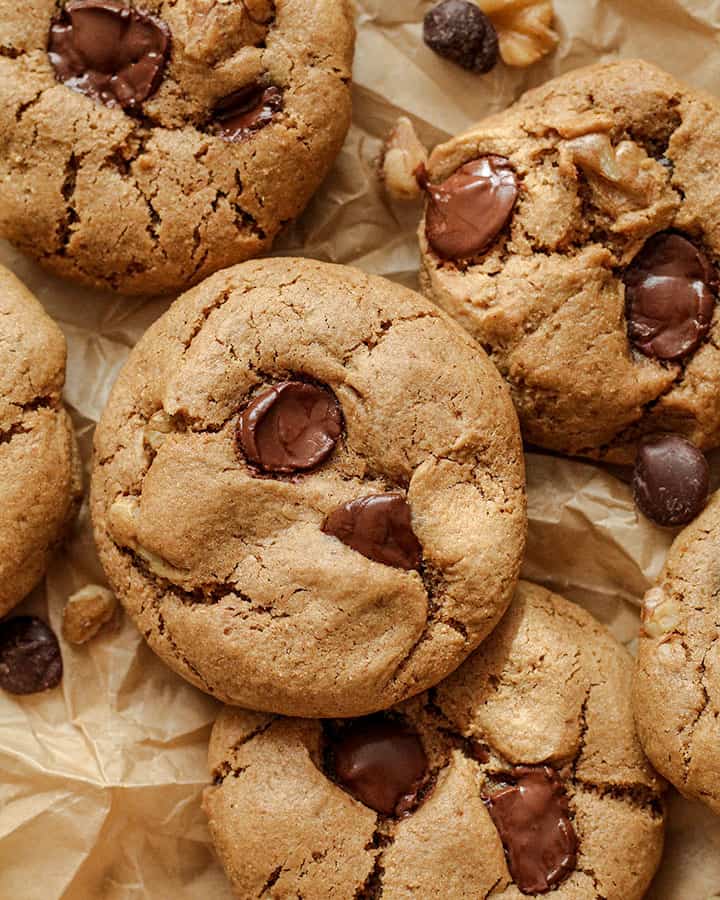 Close up of chocolate chip walnut cookies piled together on parchment paper.