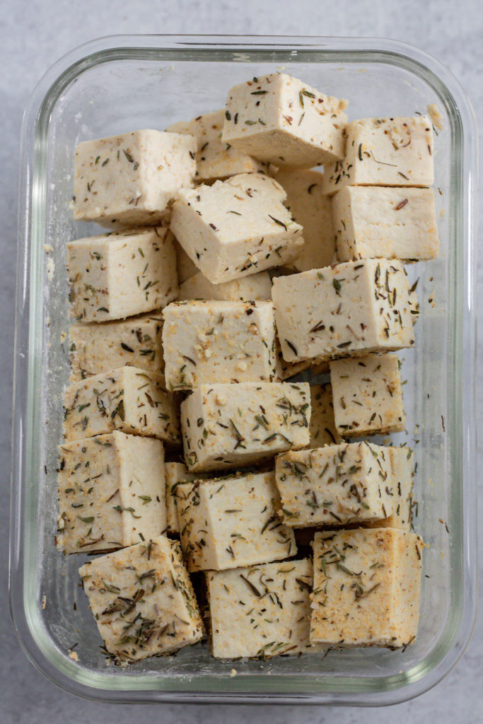 Tofu in a glass container coated with cornstarch and herbs.