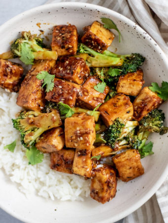 Close up shot of tofu broccoli stir fry served with white rice in a white bowl.