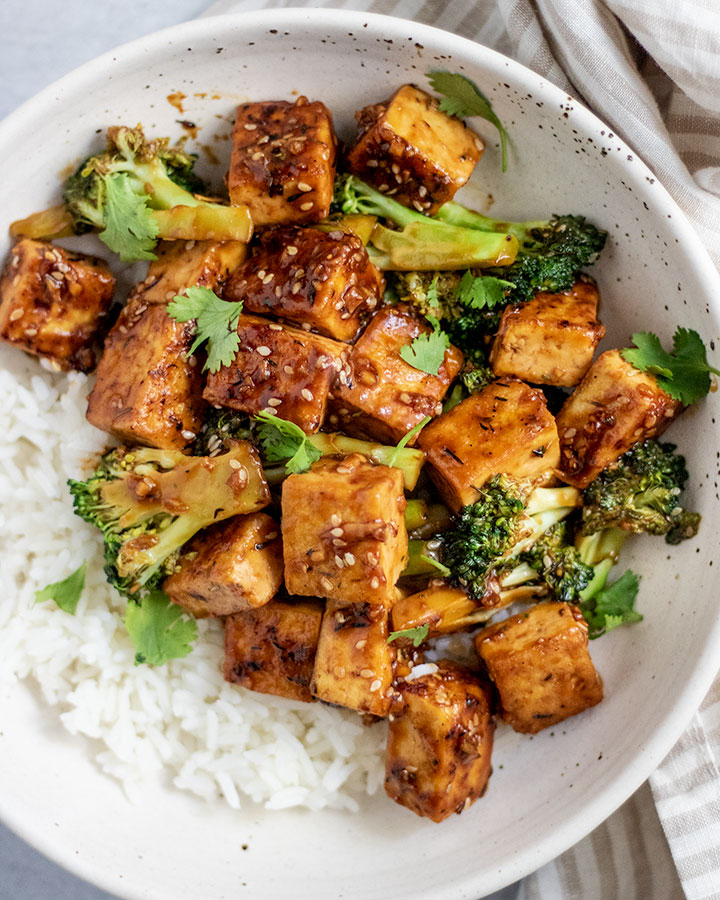 Close up shot of tofu broccoli stir fry served with white rice in a white bowl.