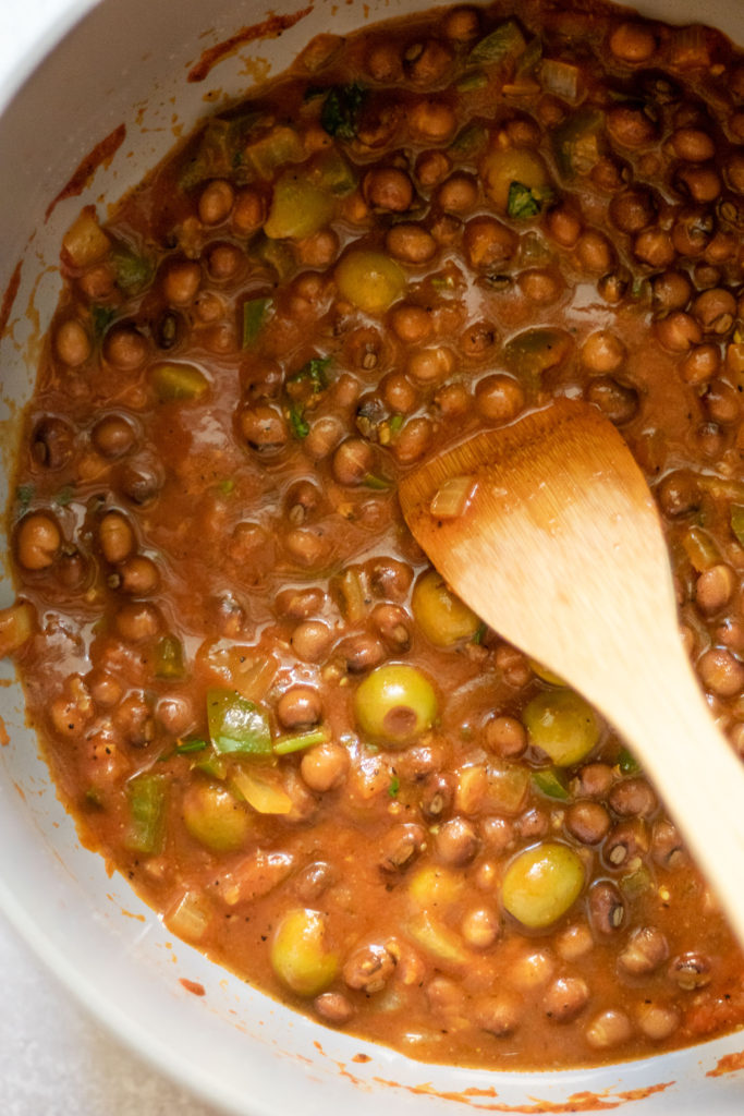 Stirring in the canned pigeon peas into the tomato sauce.