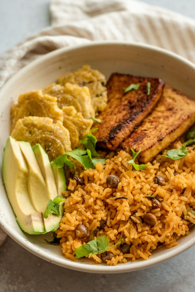 A bowl of arroz con gandules paired with avocado, tostones and pan fried tofu.