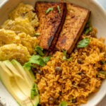 Plate of rice and pigeon peas with tofu, avocado and tostones.