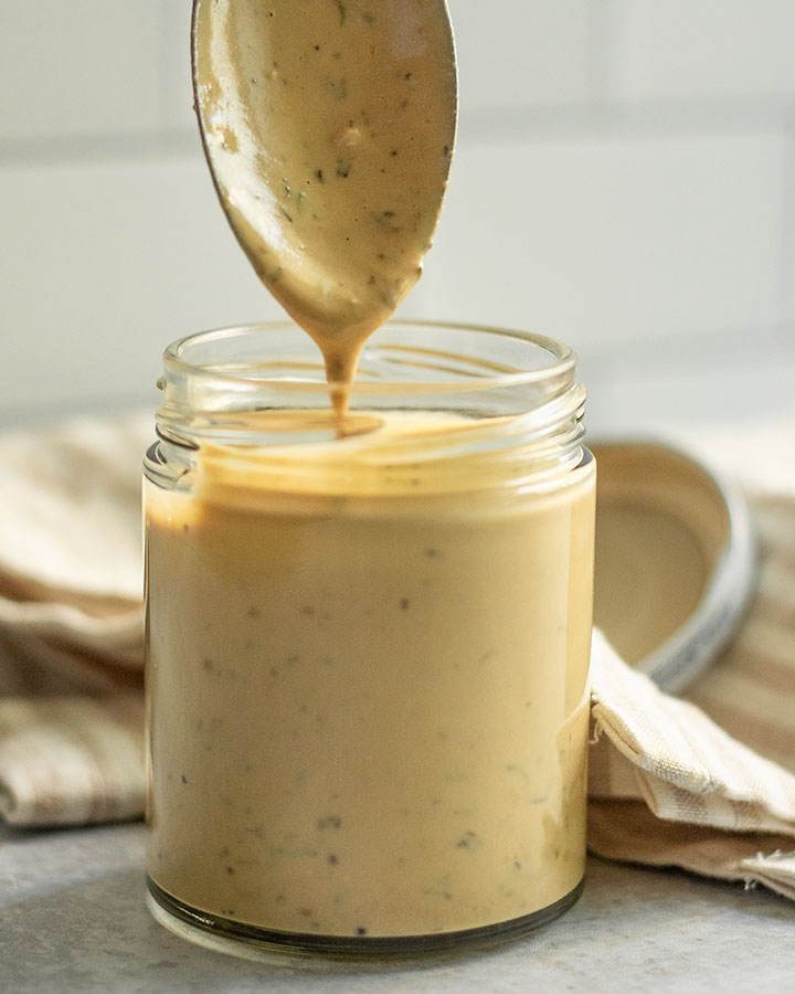 Tahini dressing being poured into a glass jar with a spoon.